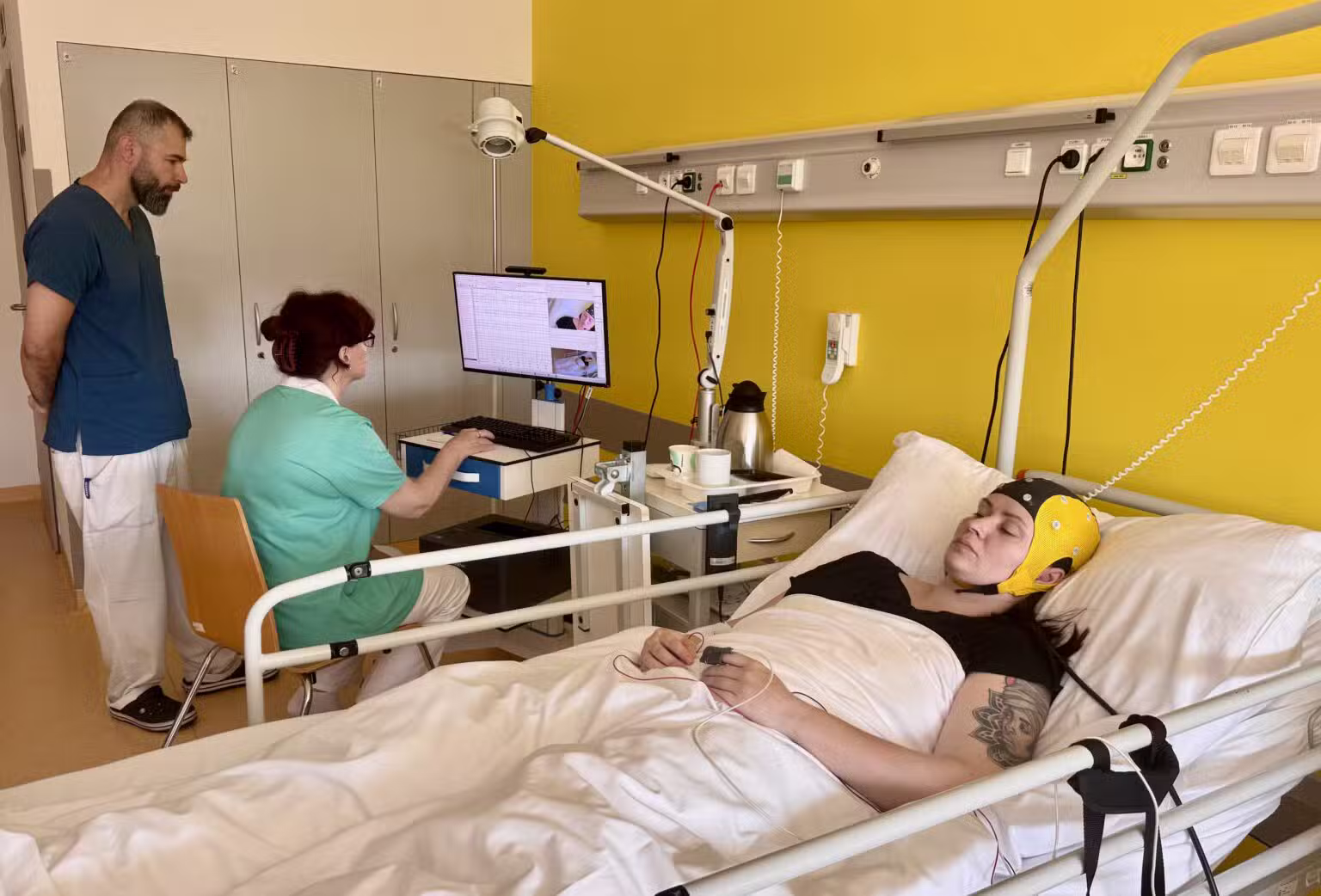 Pacientka je na lôžku v špeciálnej čiapke. Dáta získané z nej vyhodnocujú experti hneď vedľa, na monitore.